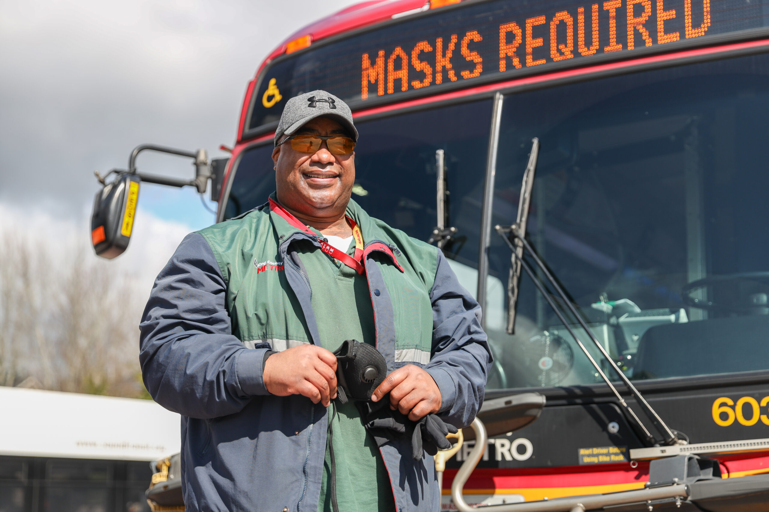 Kelvin wearing his King County Metro uniform standing in front of a Metro bus