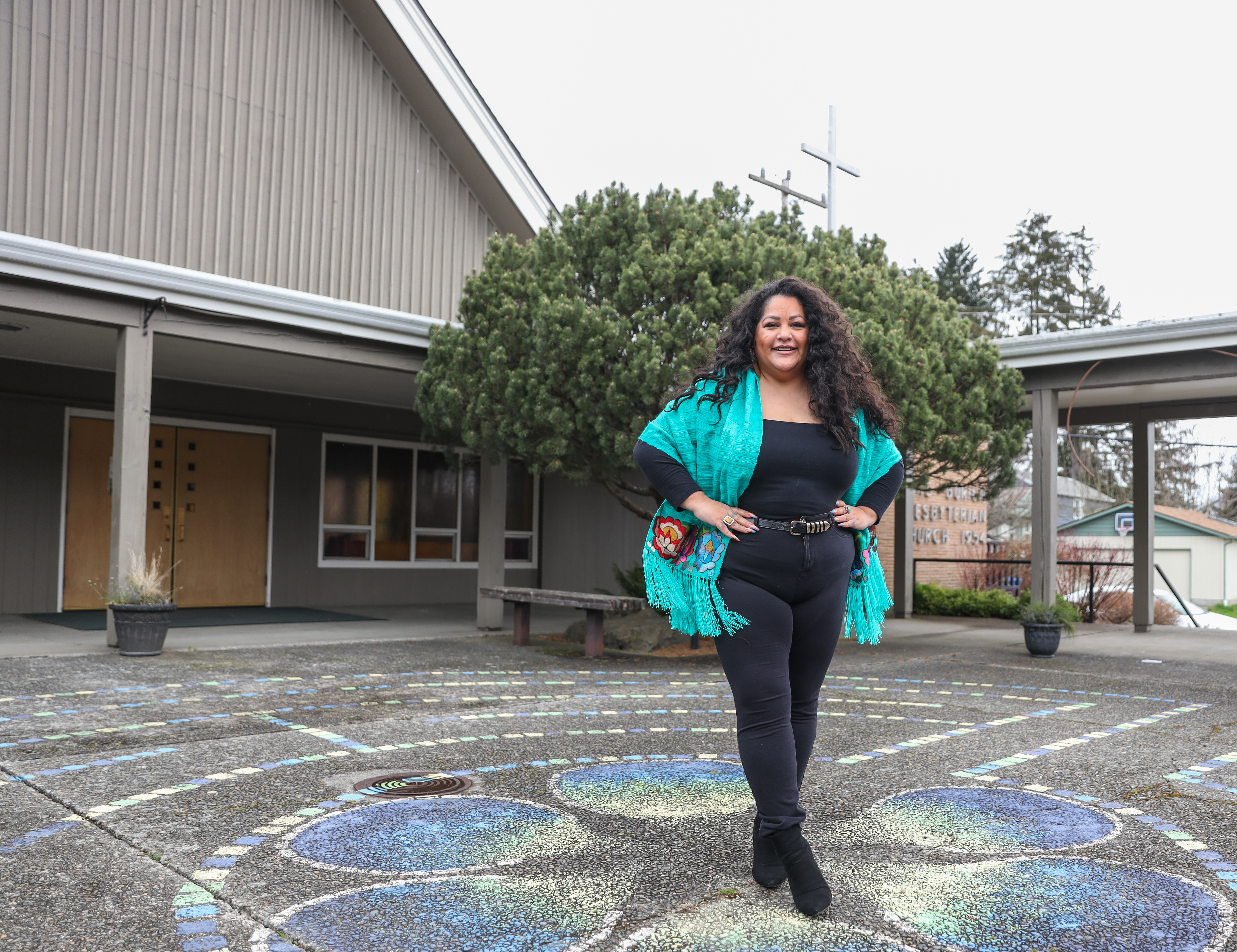 Roxana, wearing a turquoise shawl, black pants and shirt standing in front of the Lake Burien Presbyterian Church © Gates Foundation/Alex Garland