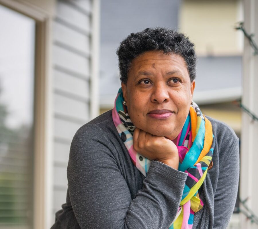 Lynda wearing a grey sweater, colorful scarf, on her front porch