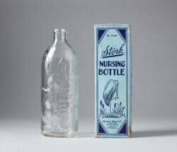 Image of a Stork brand glass baby bottle and its original blue box it was packaged in ca. early 20th century