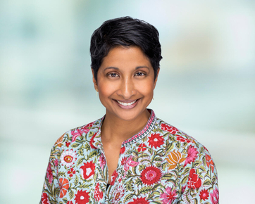 Heama wearing a bright floral shirt smiling at the camera with short dark hair.