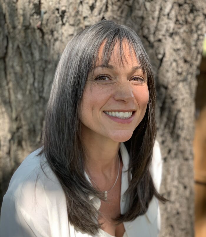 Hannah Smith smiling in front of a tree trunk wearing a white shirt.