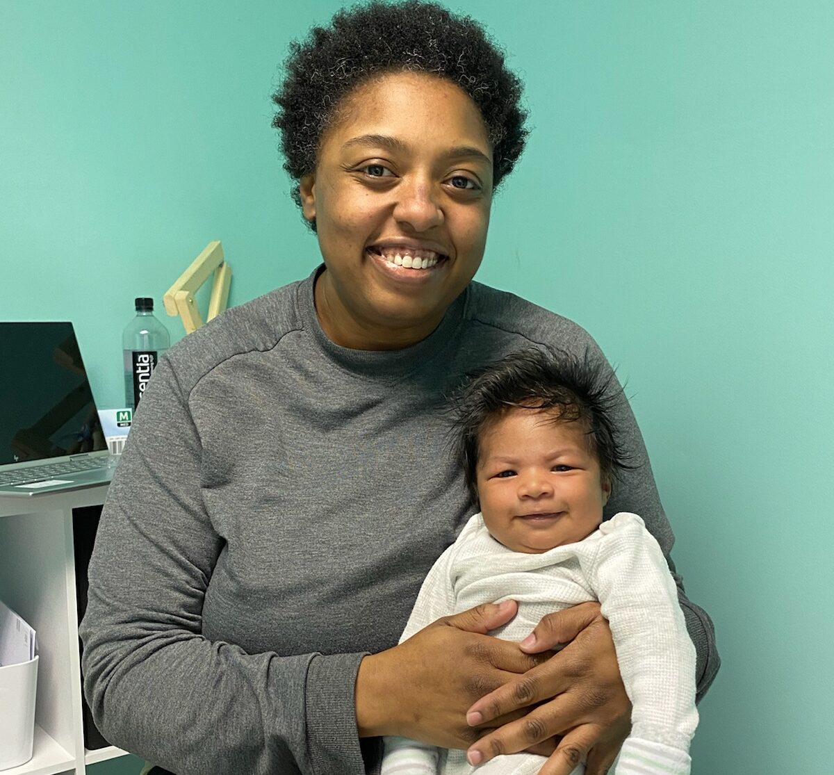 Mercedes sitting and holding a content infant in her exam room while smiling.