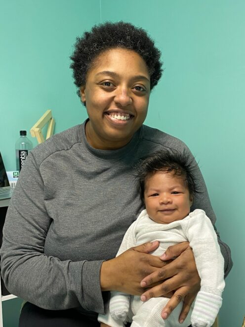 Mercedes sitting and holding a content infant in her exam room while smiling.