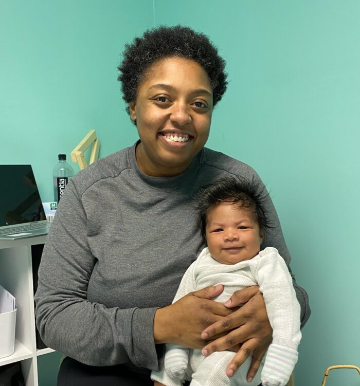 Mercedes sitting and holding a content infant in her exam room while smiling.