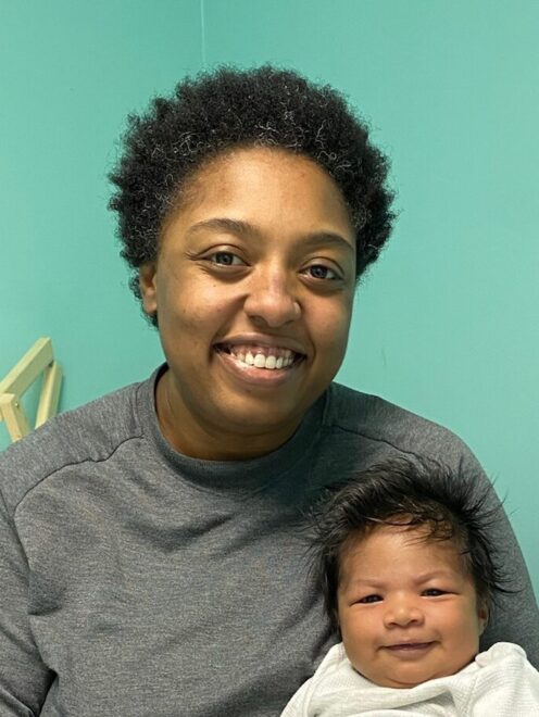 Mercedes sitting and holding a content infant in her exam room while smiling.