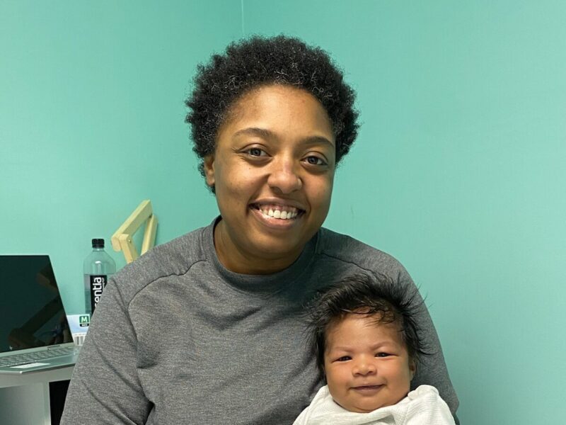 Mercedes sitting and holding a content infant in her exam room while smiling.