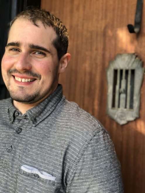 Ari wearing a gray shirt and smiling at the camera.