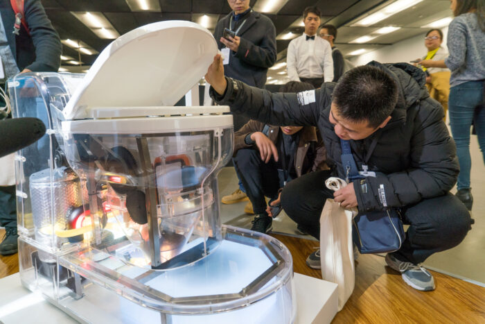 Conference visitors examining a toilet prototype inside a convention center room.