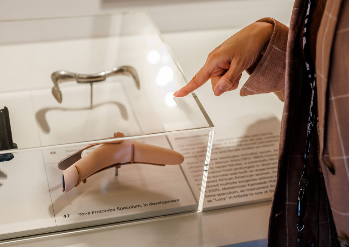A visitor points at a Yona Prototype Speculum through a case. The photo only features the woman's hand and the speculum.