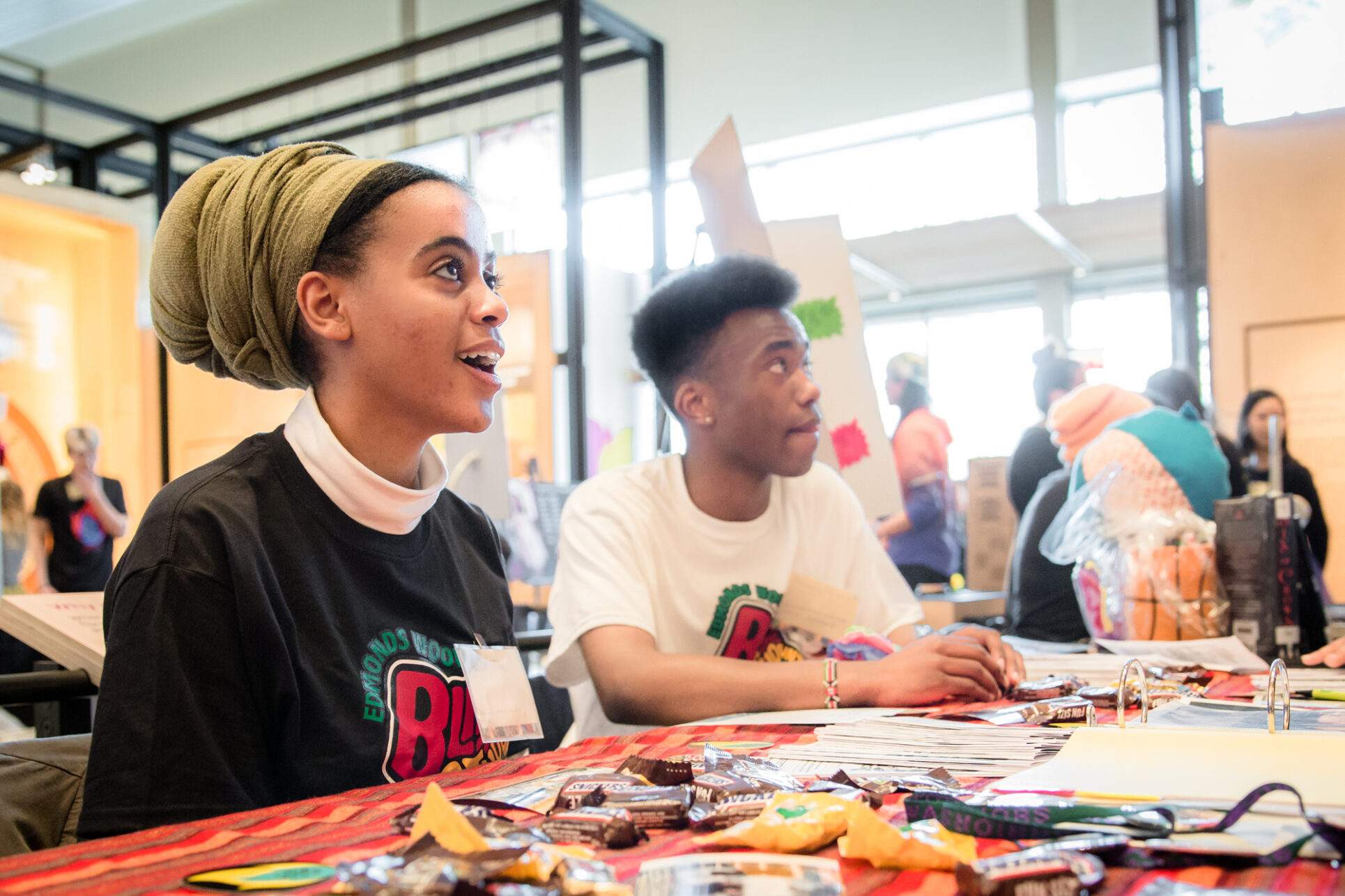 Students of Edmonds Woodway High School Black Student Union sitting and smiling at shier table at the Teen Action Fair