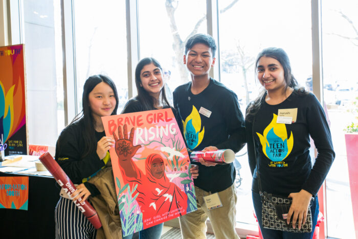 a group of teens in teen action fair shirts smiling for the camera and holding a poster.