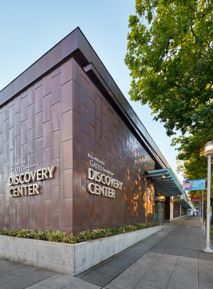 Exterior view of the Bill & Melinda Gates Foundation Discovery Center with green leafed trees lining the sidewalk in Seattle, Washington