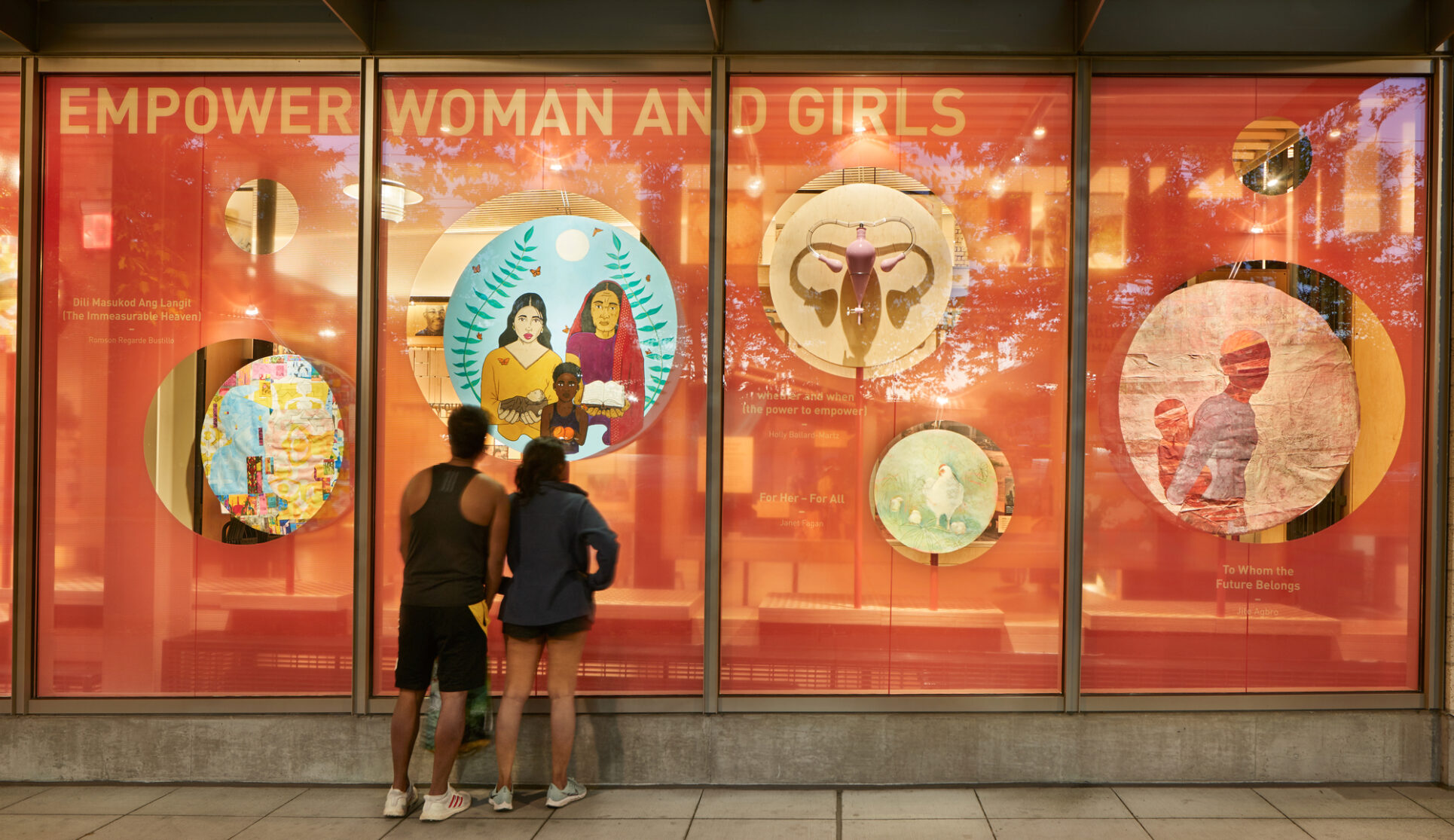 Exterior window image of the Discovery Center featuring the artwork from the Reflections exhibit with two people looking on from the sidewalk.
