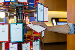 A hand places a card featuring a handwritten note about what the visitor is inspired by on the "Share Your Cause" hanging art installation at the Discovery Center.