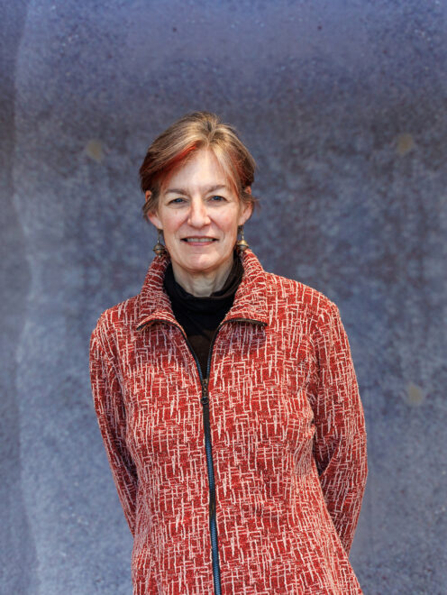 Amie Bishop standing and smiling with her hands behind her back. She is wearing a bright red coat.