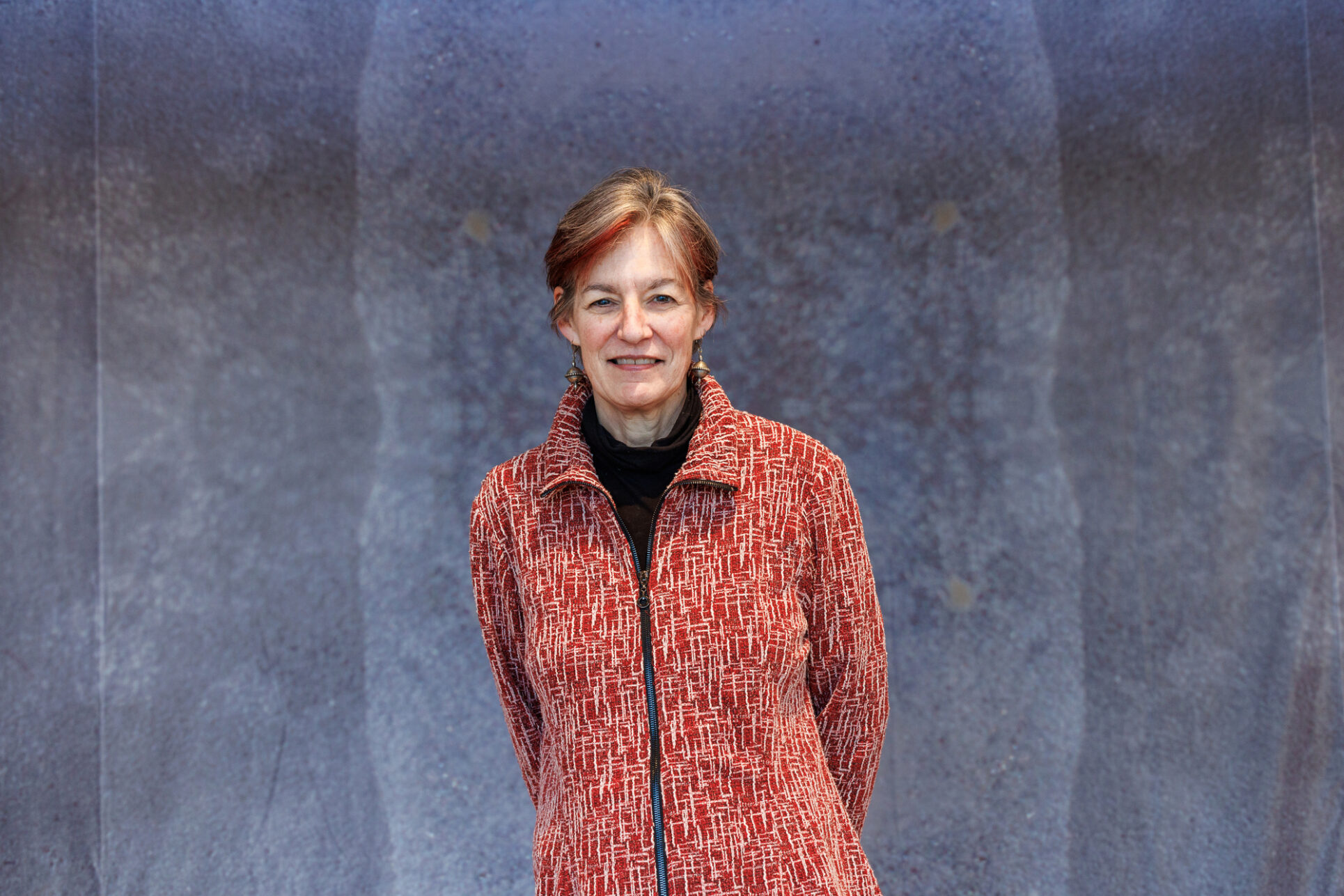 Amie Bishop standing and smiling with her hands behind her back. She is wearing a bright red coat.