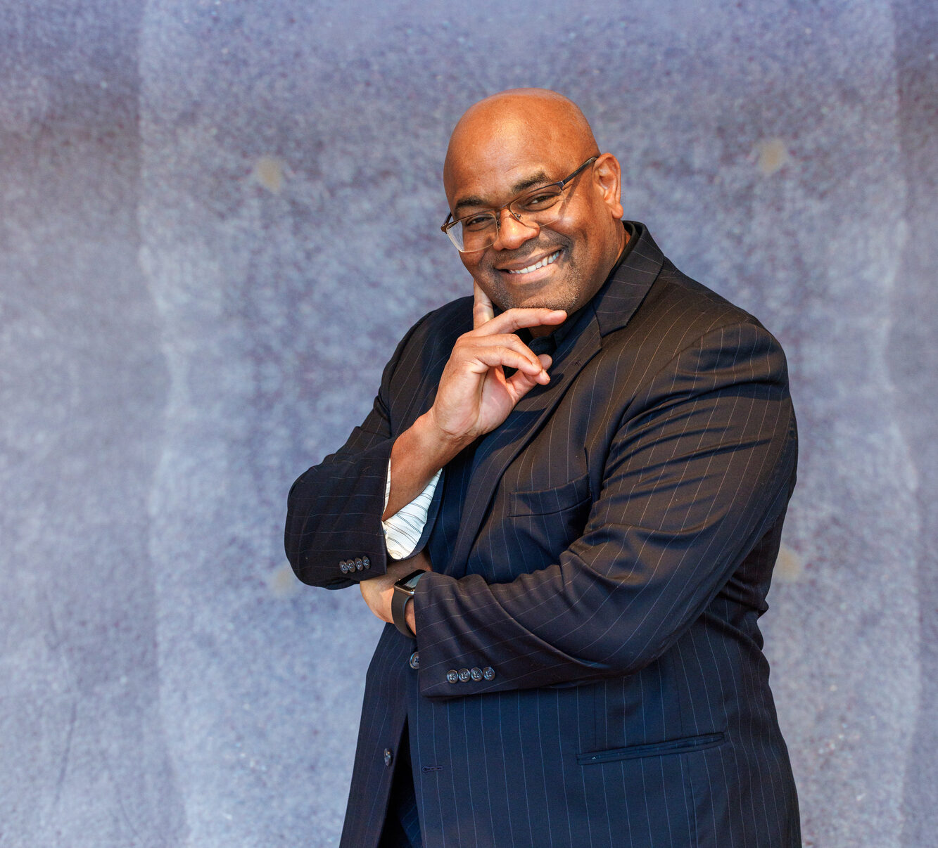 Dr. Engmann posing with his hand on his chin and smiling. He is wearing a black striped suit.