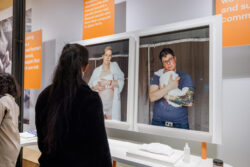 Gallery image of a visitor looking onto two portraits of a queer couple holding their newborn at the hospital