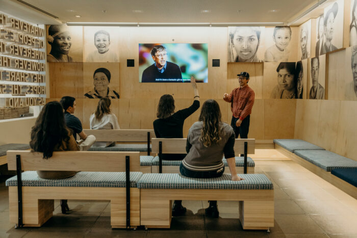 A Discovery Center staff member answers a question while visitors are seated in front of a screen in the Welcome Gallery.
