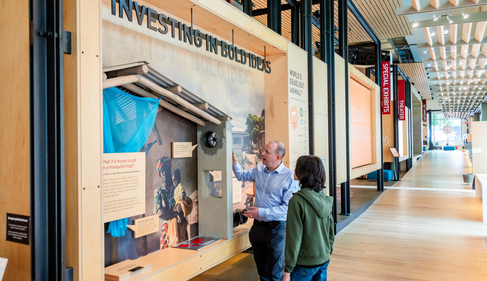A guide shows off a wall of exhibit text labeled "Investing in Bold Ideas" to a visitor in the Discovery Center.