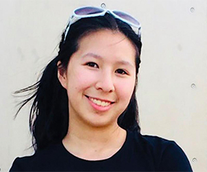 A headshot of Sarah Pham, smiling at the camera. Her hair is pulled back by some white sunglasses on top of her head and she is wearing a black shirt.