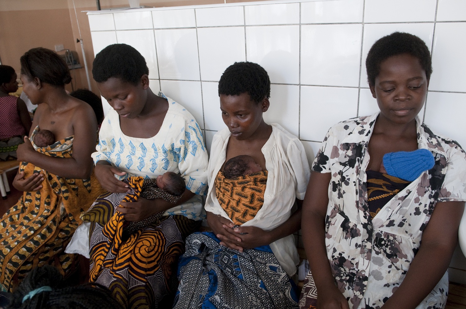 Mothers sit together on a bench in the Kangaroo Mother Care unit of a hospital.
