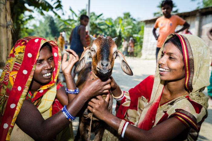 Two women hold a goat while smiling
