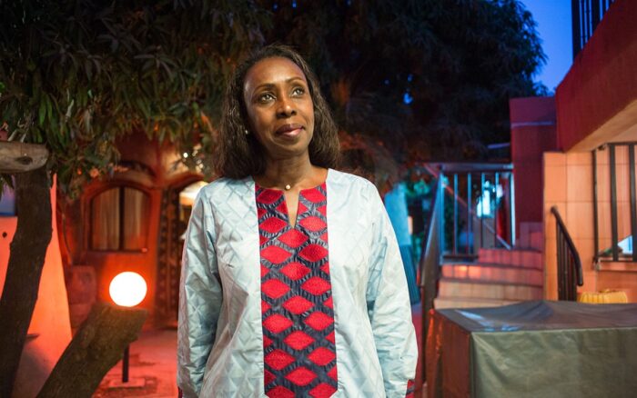 Woman in lab coat walking at dusk outside and smiling