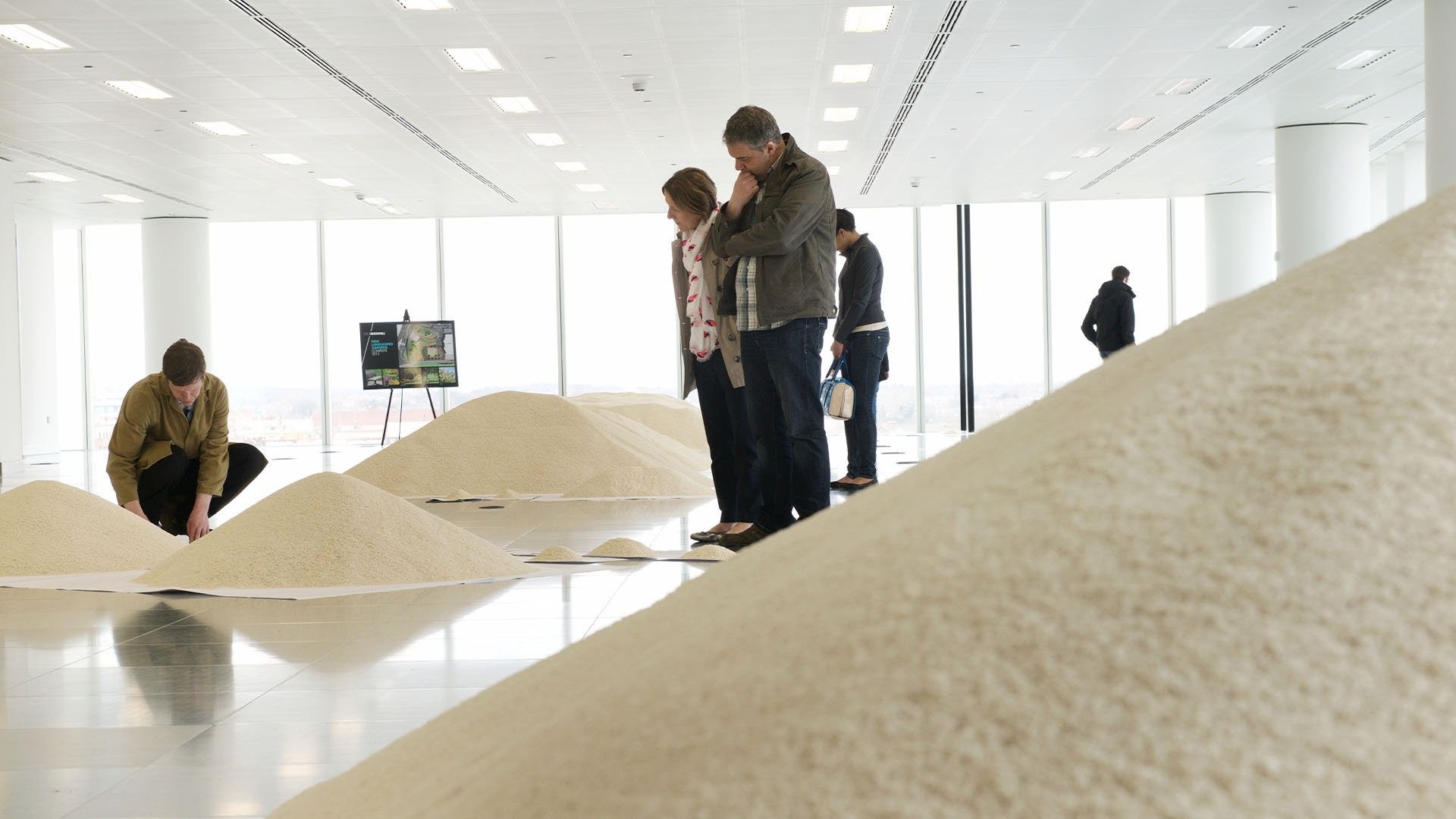 Visitors watch Stans Cafe artists transform piles of rice to demonstrate data points.